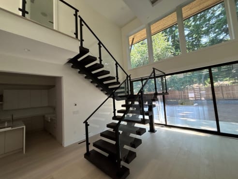 Dark wood floating stair on dual black stringers with post-to-post glass railing turning at a landing in a bright great room