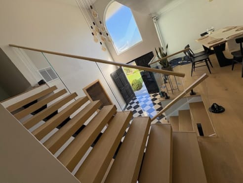 White oak floating stair with glass railing and wood handrail descending toward an arched entry