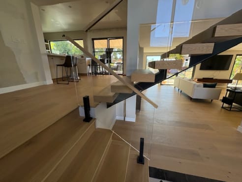 Floating oak treads on a black stringer with frameless glass and wood handrail in a bright great room