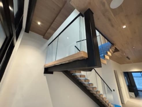 Floating switchback landing in a black frame with frameless glass under a white oak ceiling