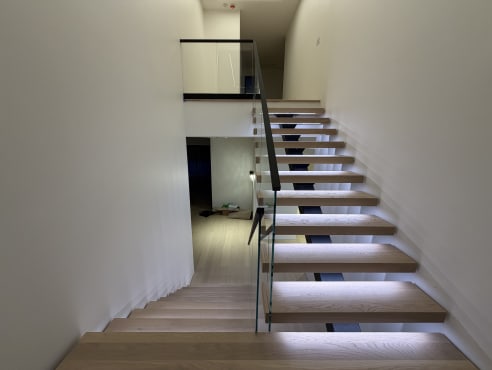 Floating oak stair with LED-lit treads, glass railing and a base rail glass landing above