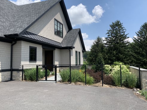 Black cable railing fence and gate border a planted garden beside an asphalt drive