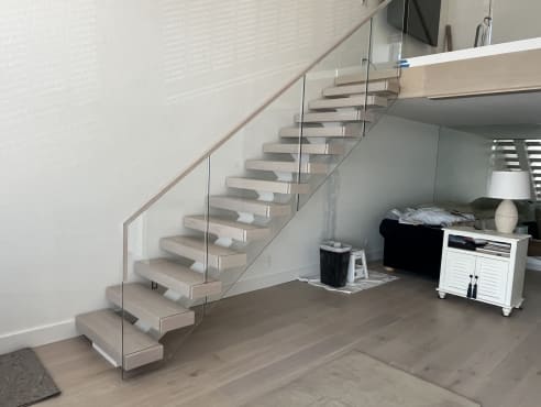 Whitewashed oak floating treads with frameless glass and oak handrail rising to a loft