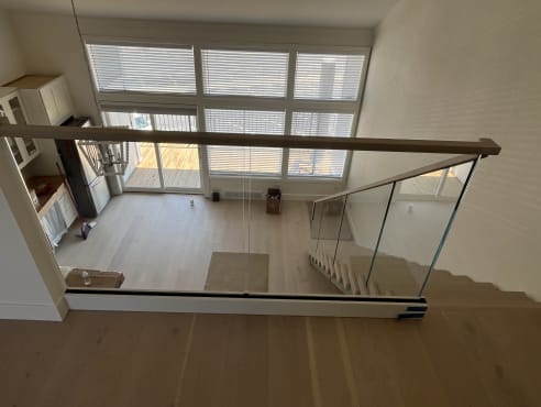 Frameless base rail glass with a whitewashed oak cap overlooks a sunlit living room