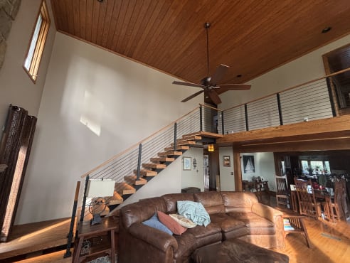 Pine floating treads on a black mono stringer with black cable railing and pine handrail rising to a loft under a tongue-and-groove ceiling