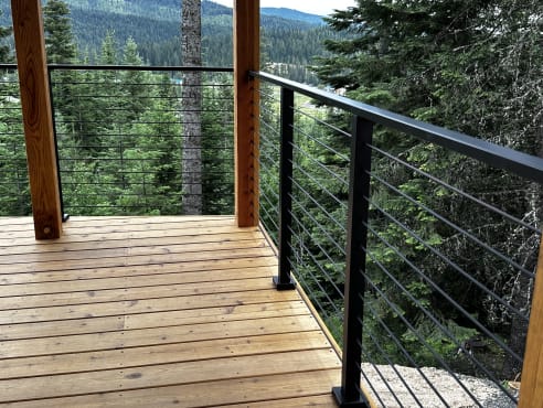 Black cable railing at the corner of a cedar deck with timber posts and evergreen forest views.