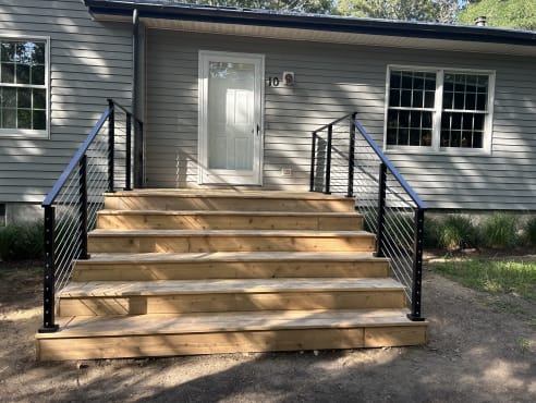 Black cable railings flank wide cedar entry steps on a gray-sided ranch home.