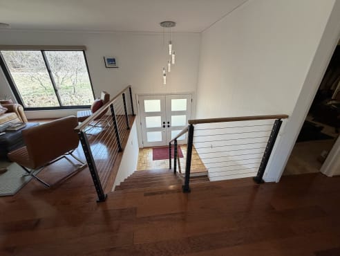 Black-post cable railing with wood handrail wraps a stair opening down to a bright entry with glass double doors.
