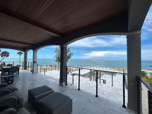 Black posts and horizontal stainless cables edge a covered marble veranda framed by arches with an ocean view.