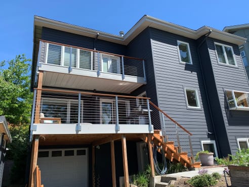 Stainless cable railing lines stacked balconies and an exterior stair on a dark-sided home.
