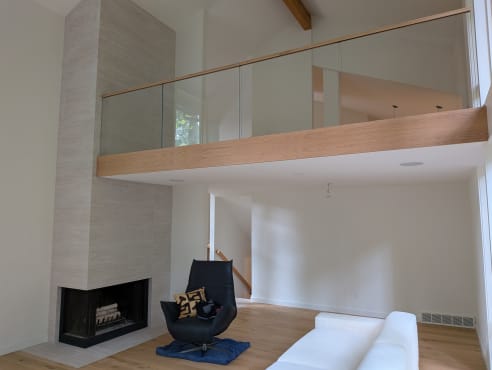 Frameless glass with a wood cap rail and no visible hardware edges a loft above a living room with a corner fireplace.
