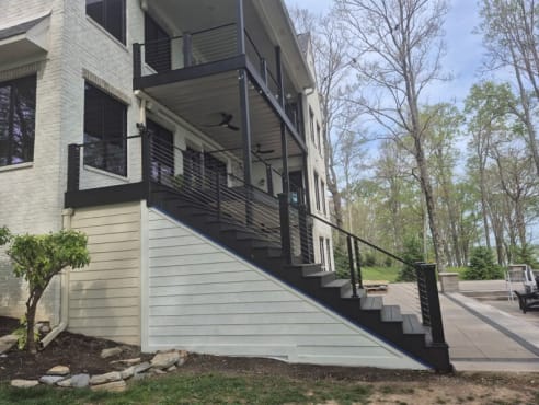Dark cable railing runs along a long exterior stair and stacked decks on a white brick lakeside home.