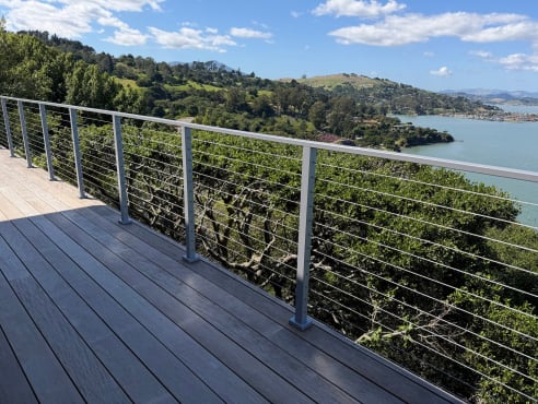 Silver aluminum cable railing on a composite deck overlooking green hills and a bay.