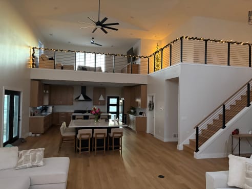 Black cable railing with a wood cap follows a stair and wraps a loft above an open kitchen and living room.