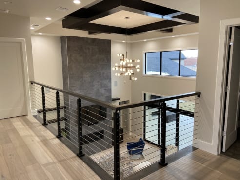 Black posts and top rail with stainless cable infill around a second-floor opening with a modern chandelier.