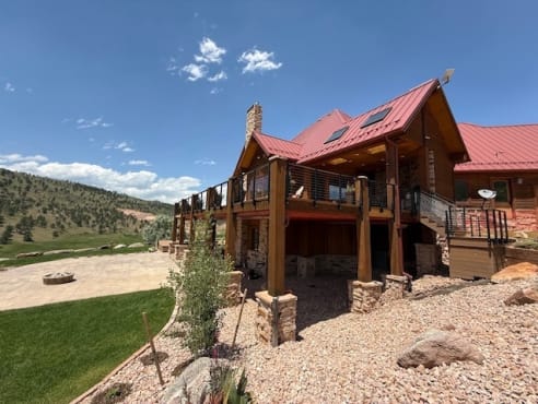Wide view of a red-roofed lodge with a wraparound deck finished in black cable railing.