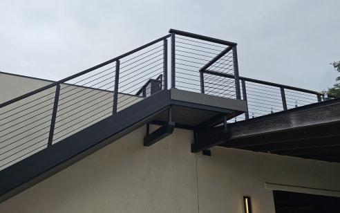 Black cable railing on a steel exterior stair and landing against a stucco wall