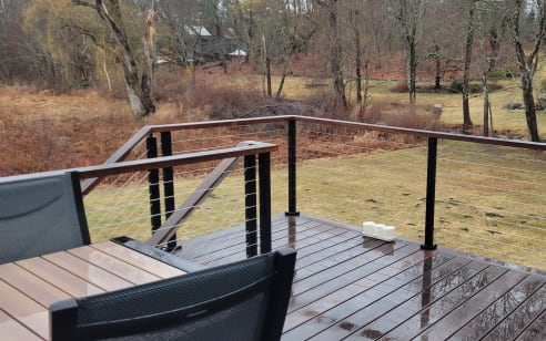 Black cable railing with Ipe top rail around a wet hardwood deck overlooking a wooded yard.