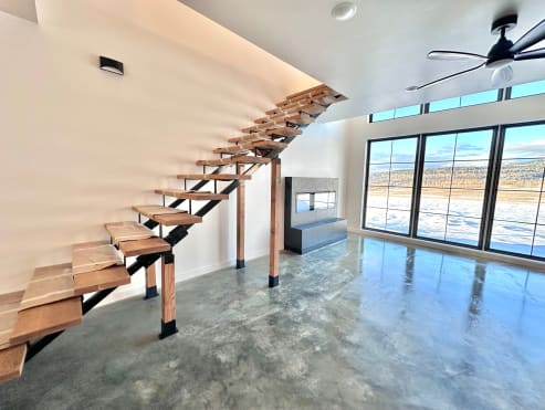 Black mono stringer floating stair with chunky live-edge wood treads in a bright room with polished concrete floors and lake views.