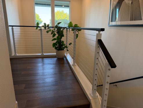 White posts with stainless cables and a black top rail frame an upstairs landing with a potted plant.