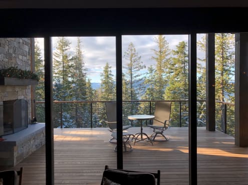Black rod railing with wood cap around a covered ipe deck with stone fireplace and forest view.