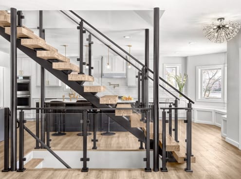 Black FLIGHT mono stringer with rustic oak treads and black post-to-post glass railing in front of a bright white kitchen.
