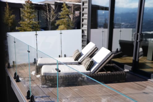 Frameless glass on black talons edges a composite deck with two loungers beside a modern home.