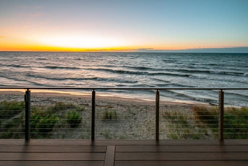 Bronze posts and cable infill line a composite deck above a sandy beach as the sun sets over the lake.