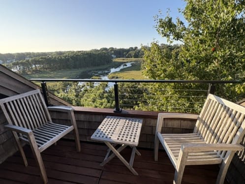 Black cable railing on a compact balcony with teak chairs overlooking a salt marsh.