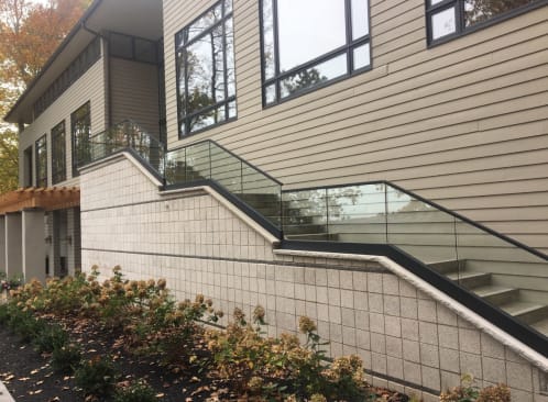 Frameless glass with a black cap rail steps along a block retaining wall and exterior stair beside a modern home.