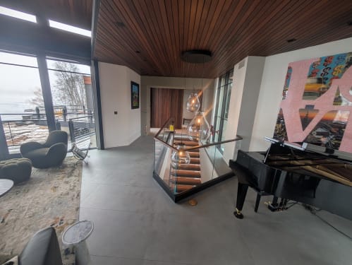 Base rail glass with a walnut cap wraps a lit stair opening beside a grand piano and lake view