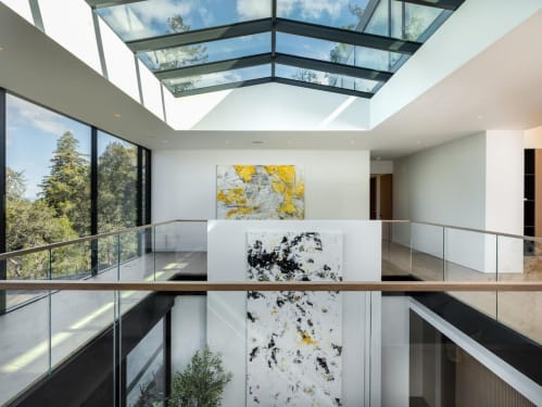 Glass railing with a white oak cap rail encircles an open atrium beneath a large skylight with forest views.