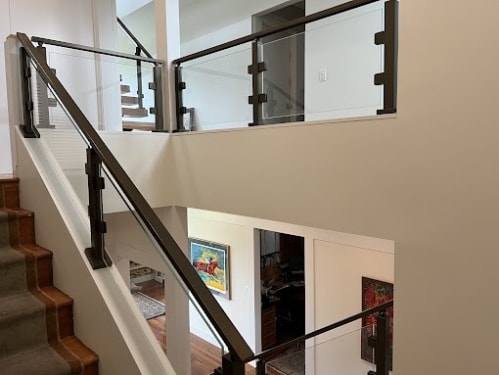 Glass panels between dark bronze posts follow a carpeted stair and wrap an upper landing.