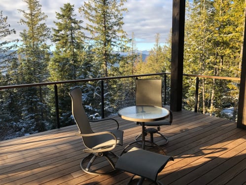 Black rod railing with wooden cap around an ipe deck with patio chairs overlooking a forested valley.