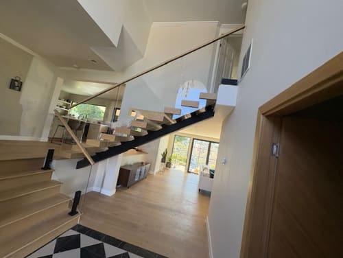 White oak floating stair with glass on talons and a wood handrail overlooking an open living room