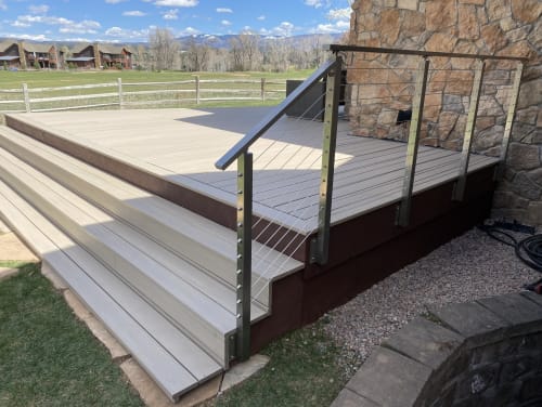 Stainless steel side-mount posts with cable infill line a composite deck stair with mountain views.
