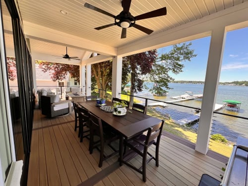 Black cable railing guards a covered porch with a dining table overlooking a lake and docks.