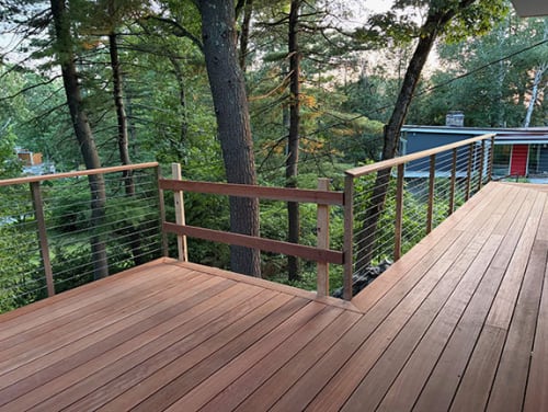 Cable railing with wood cap rails follows a hardwood deck wrapping around trees.