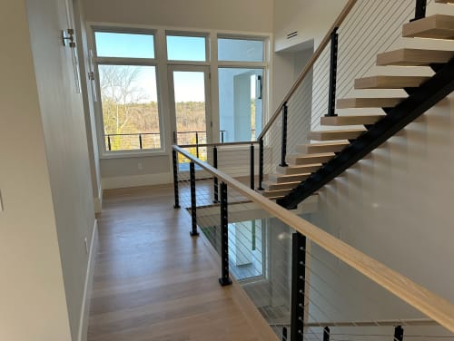 White oak treads on a black mono stringer with cable railing and oak handrail beside tall windows.