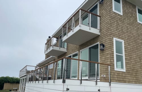 Side-mounted cable railing with wood top rail on balconies and a deck of a cedar-shingle home.