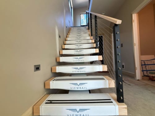 Floating stair in clean Viewrail tread covers with black cable railing and maple handrail