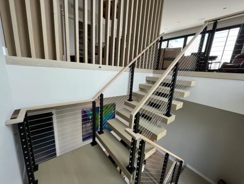 Whitewashed oak FLIGHT Mono switchback with black cable railing and pale oak handrail beside a slat screen