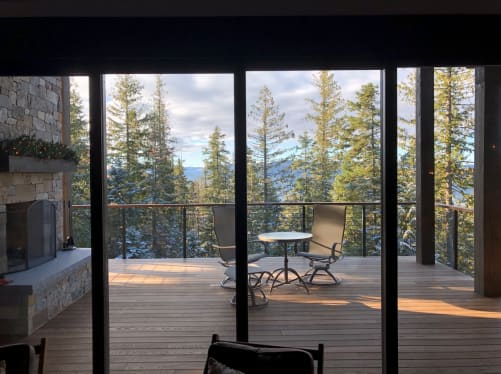 Black rod railing with wood cap around a covered ipe deck with stone fireplace and forest view.