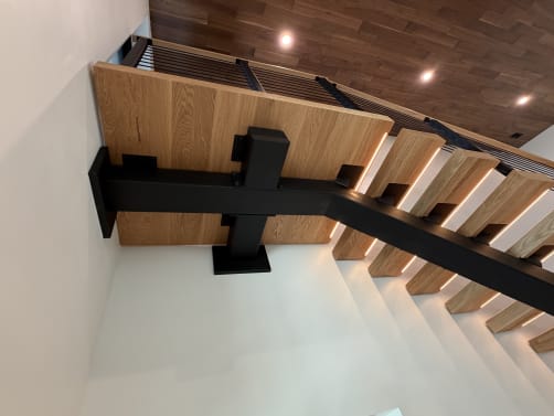 Black mono stringer and post supporting thick white oak treads with LED lighting