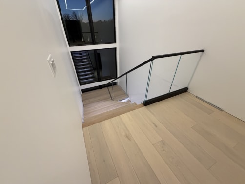 Frameless base rail glass with a black cap wraps a stair opening on pale oak floors