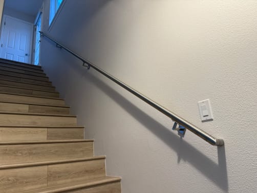 Brushed stainless round handrail on wall brackets climbing a pale-oak stair