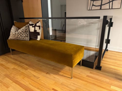 Black-framed glass railing and gate along a hardwood landing next to an upholstered bench.