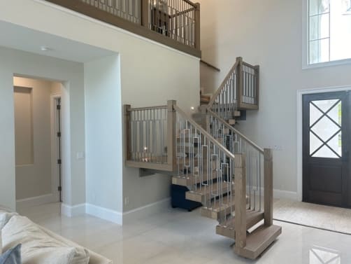 Oak mono stair with wood newels and geometric balusters turns at a landing next to a dark front door.