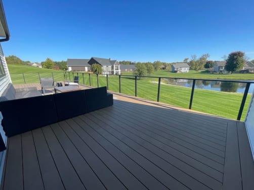 Black cable railing surrounds a wide composite deck overlooking a pond and neighborhood lawns.