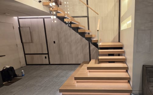 Floating oak stair with LED-lit treads and glass railing climbing a paneled wall in a modern living space